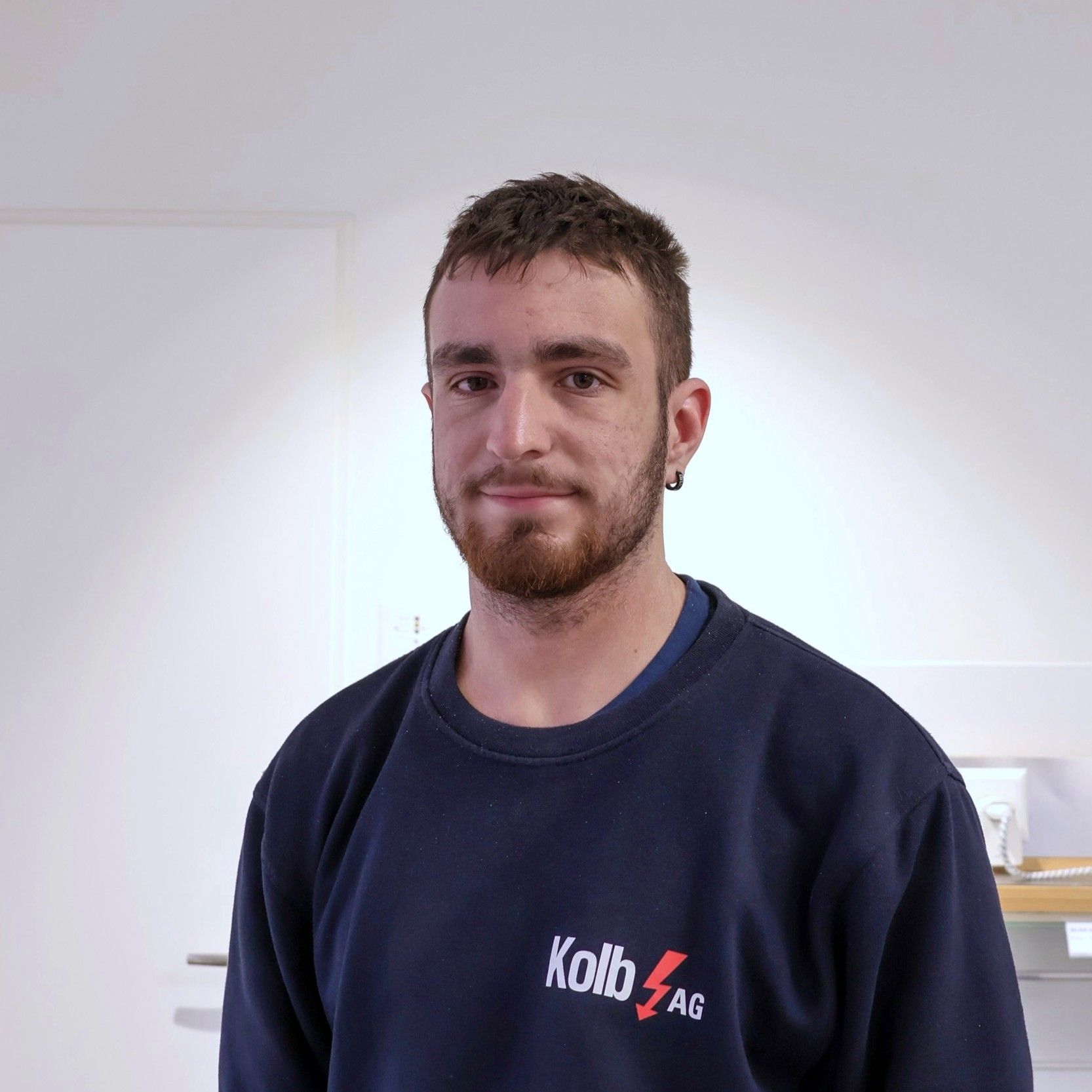 Ein Mann mit Bart und einem dunkelblauen Sweatshirt der Kolb AG steht drinnen.