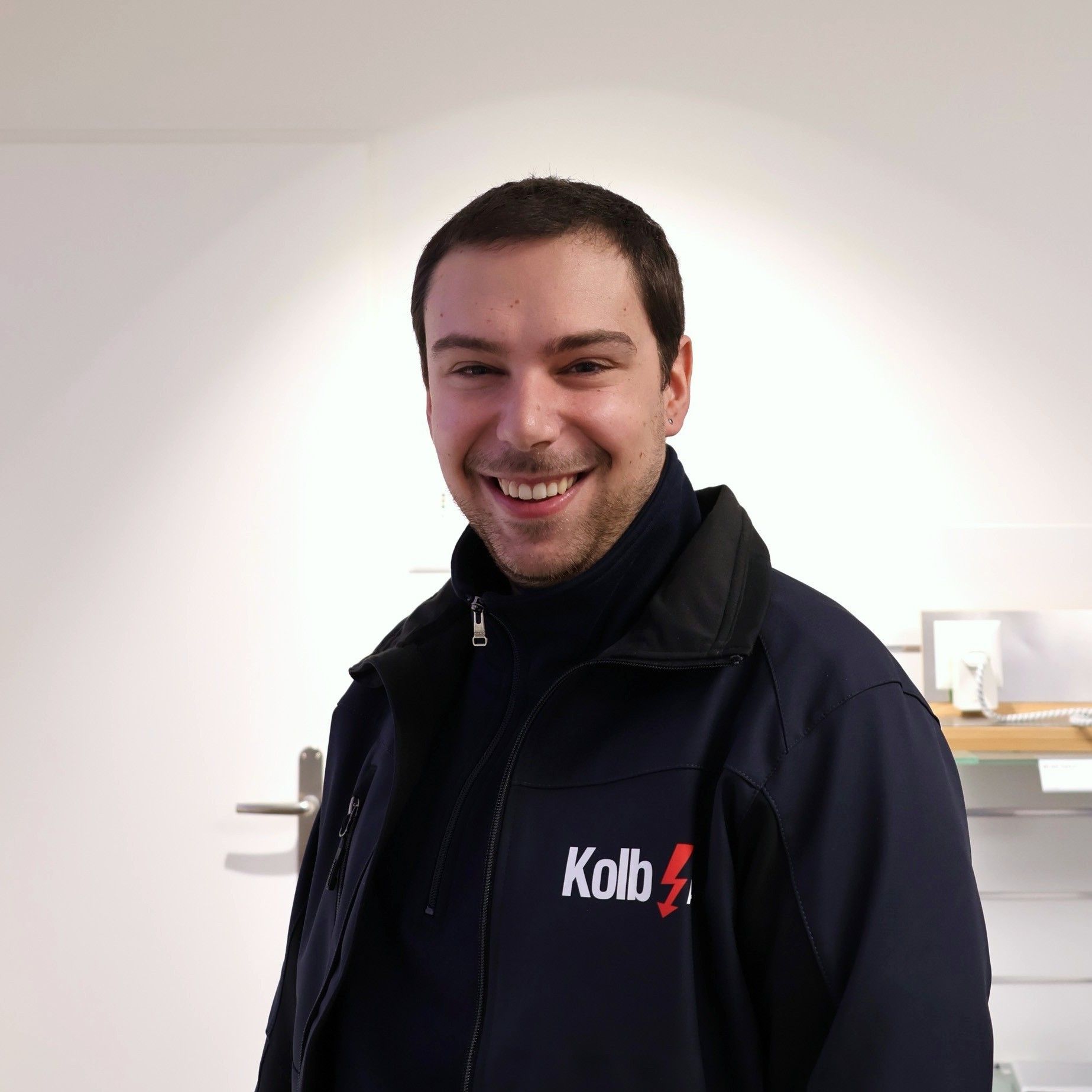 Mann mit einem freundlichen Lächeln, trägt eine marineblaue Jacke mit dem „Kolb“-Logo.
