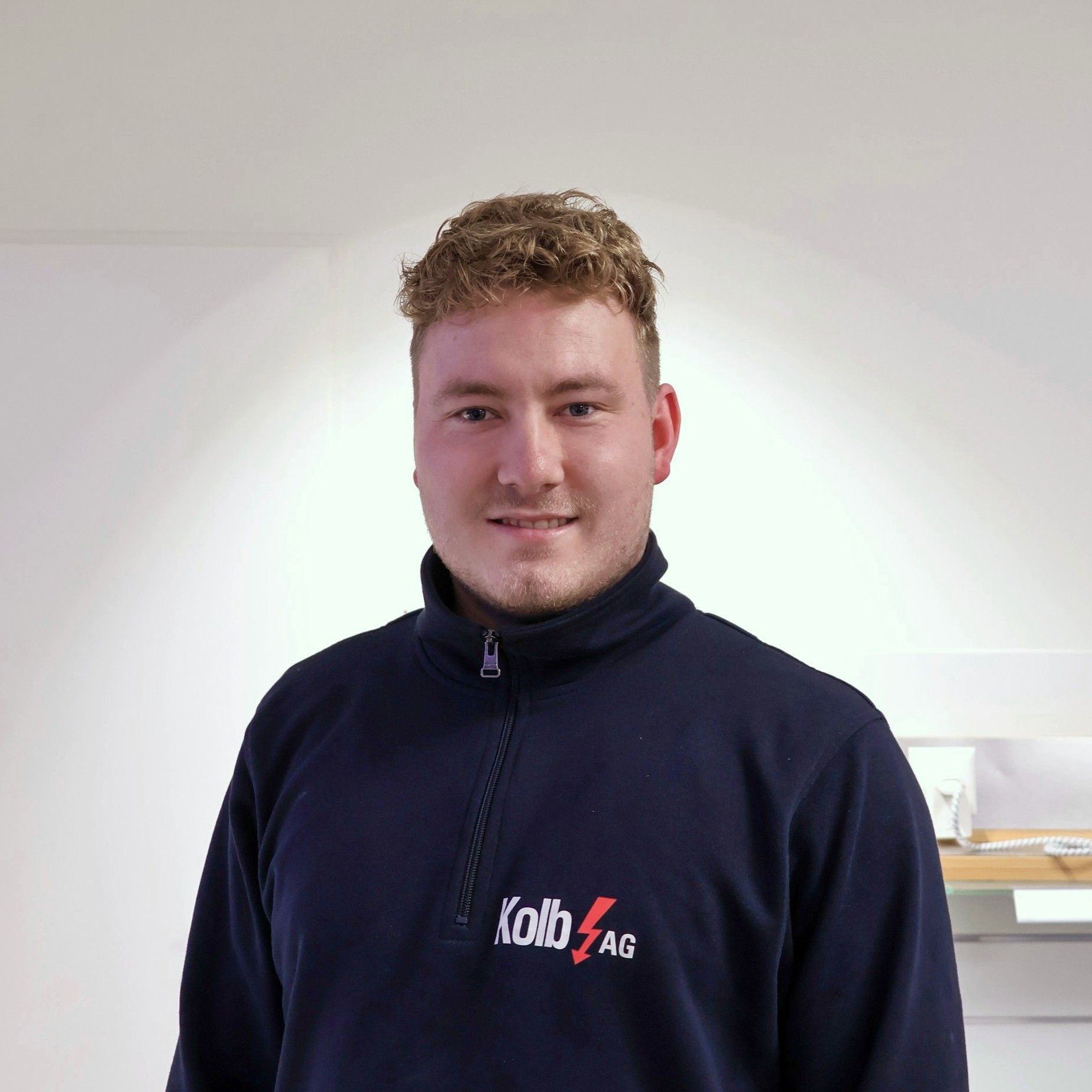 Mann im dunkelblauen Sweatshirt, lächelnd; weißer Hintergrund. „Lob AG“-Logo auf dem Shirt.