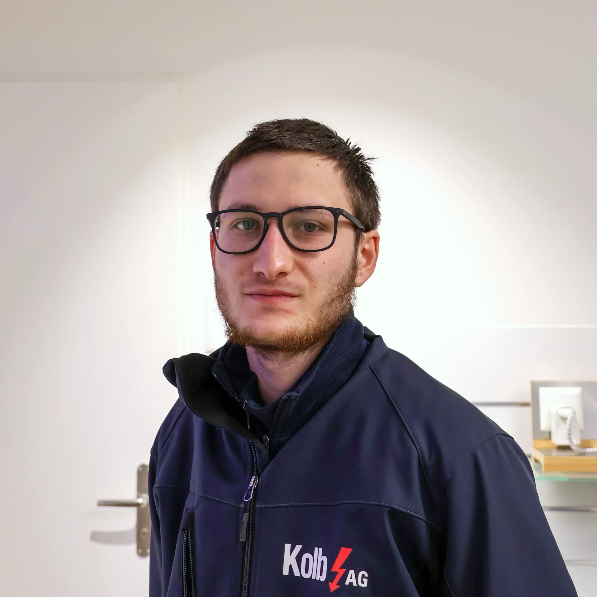 Ein Mann mit Brille und einer marineblauen Jacke mit dem Logo „Kob AG“ steht in einem Geschäft und blickt in die Kamera.