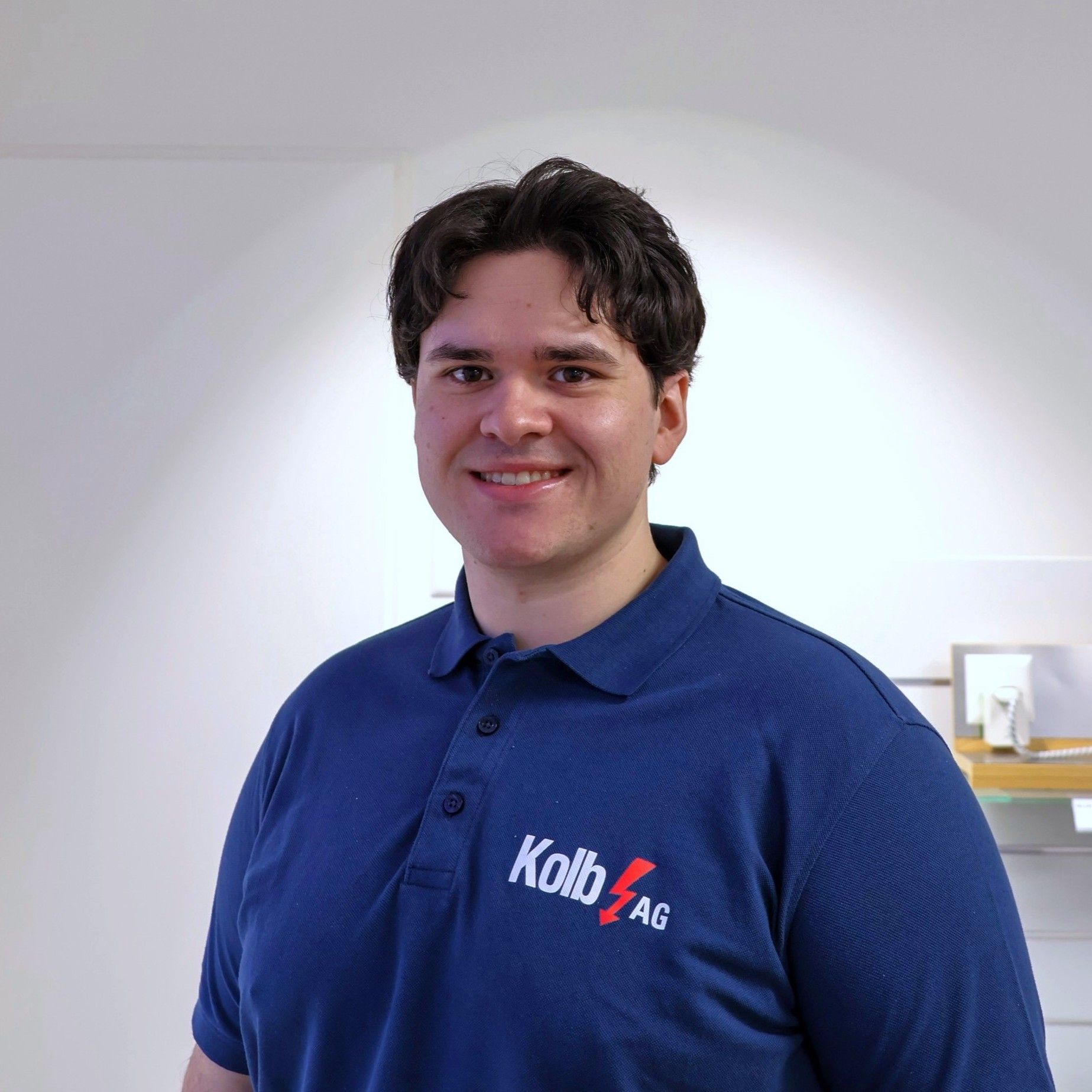 Mann im blauen Hemd, lächelnd, Logo „Kolb AG“, drinnen, helle Haut.