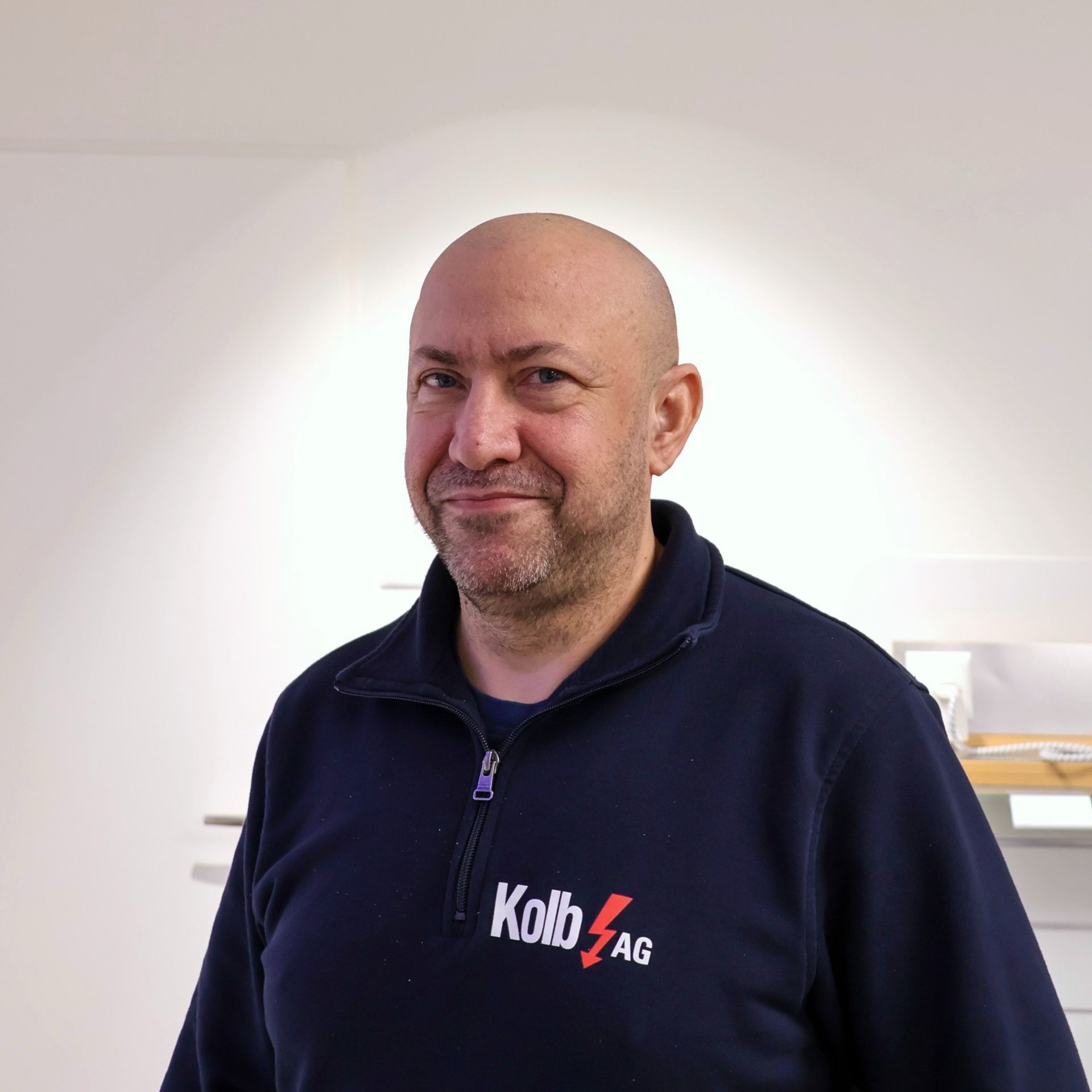Glatzköpfiger Mann mit Bart, blauem Pullover, Logo der Kolb AG.