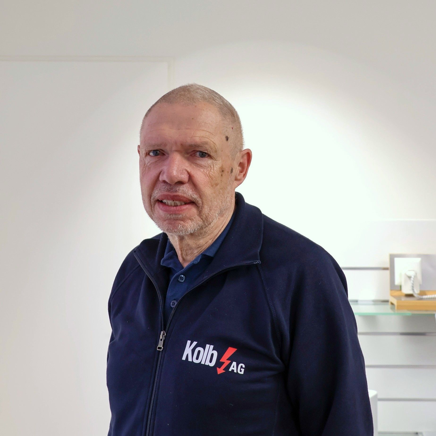 Mann in einem blauen Sweatshirt mit Logo steht in einem Geschäft.