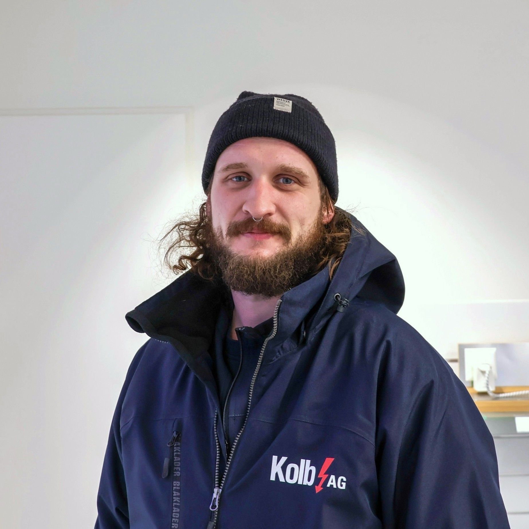 Mann mit Bart, schwarzer Mütze und blauer Jacke, lächelt drinnen.