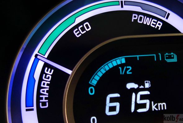 Aufladen eines Elektrofahrzeugs mit einem schwarzen Kabel; heller Sonnenuntergang im Hintergrund.