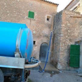 Un camión cisterna azul está estacionado frente a un edificio de piedra.