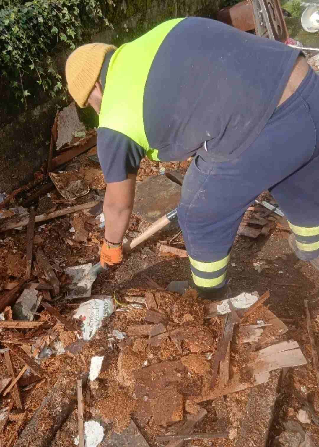 Un trabajador con chaleco reflectante y casco de seguridad retirando escombros de un suelo dañado.