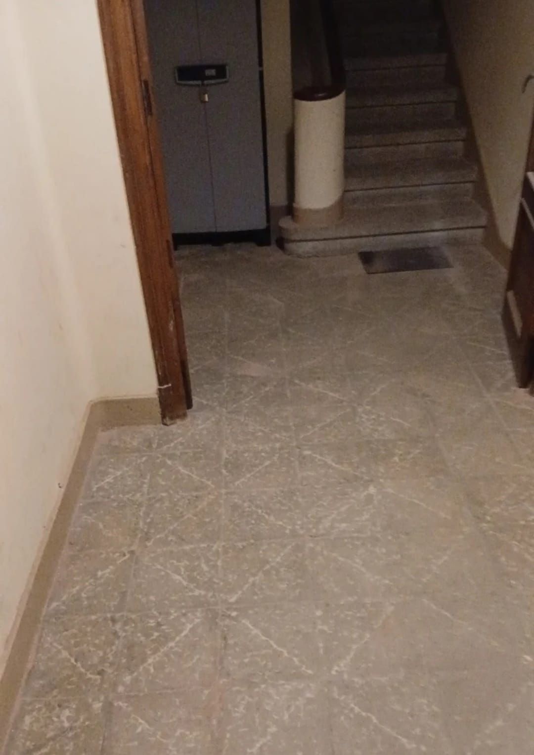 Pasillo estrecho con suelo de baldosas que conduce a una escalera y al marco de una puerta a la izquierda.
