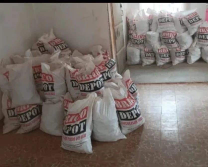Sacos blancos apilados con etiquetas rojas en una habitación pequeña, junto a un suelo de baldosas y un espejo de pared.