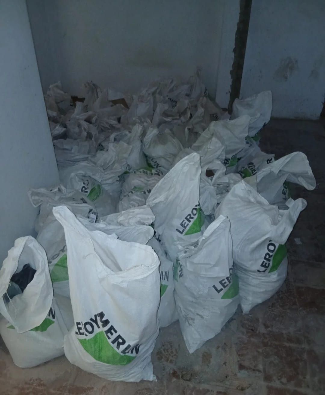 Habitación llena de sacos de plástico blancos amontonados en el suelo, junto a una pared y una puerta.
