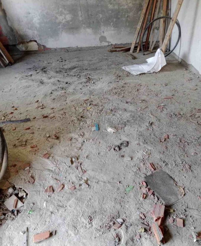 Habitación polvorienta sin terminar, con suelo de hormigón, escombros esparcidos y herramientas apoyadas contra la pared.