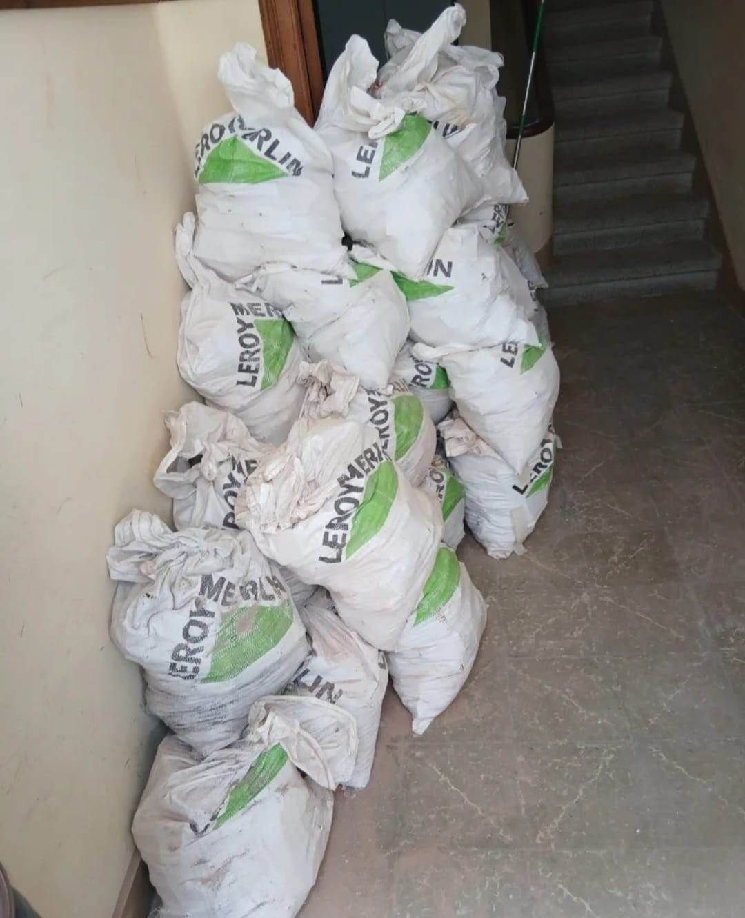 Sacos blancos apilados con provisiones, alineados junto a una pared del pasillo cerca de una escalera.