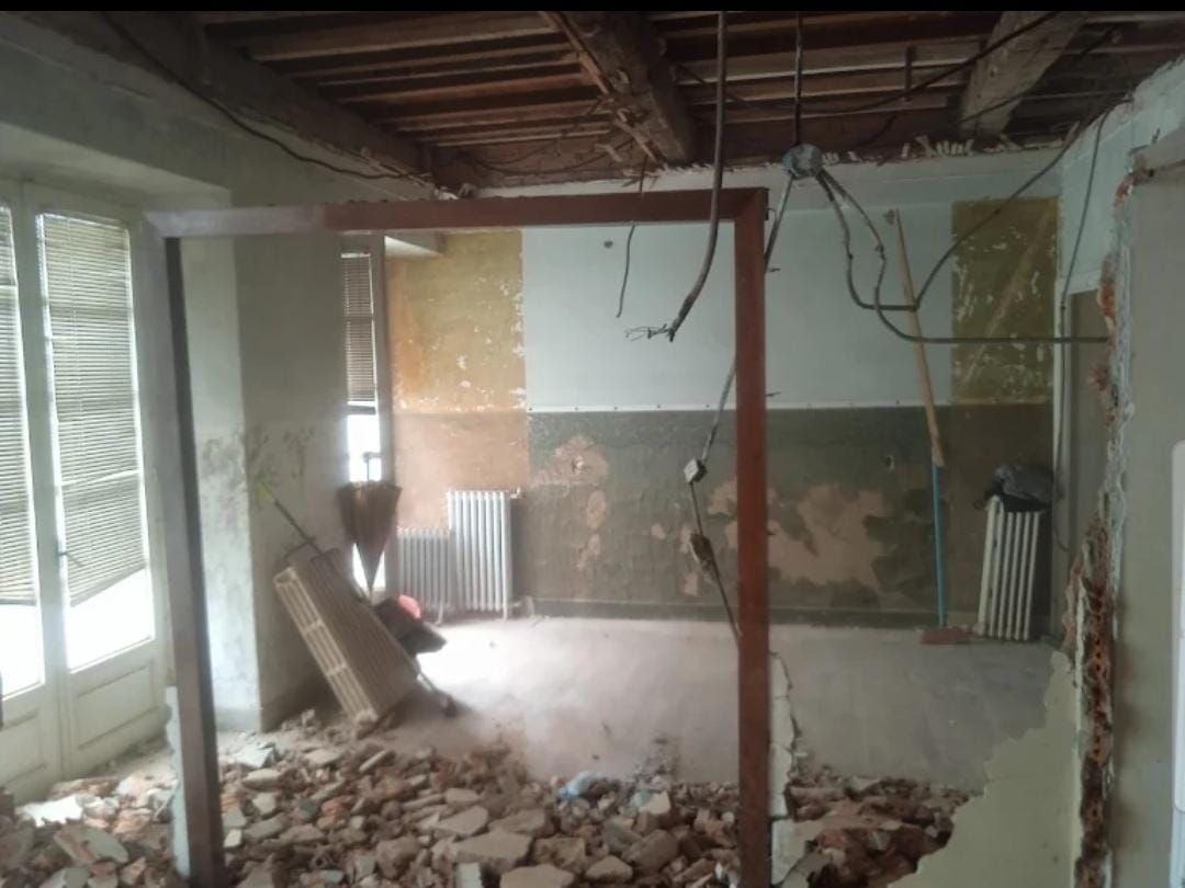 Habitación renovada con escombros en el suelo, cables a la vista en el techo y paredes dañadas
