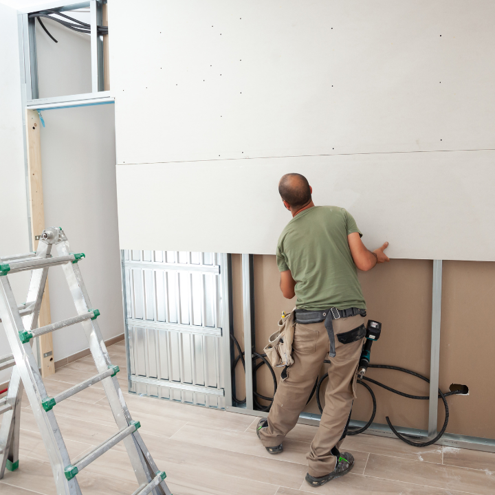 Obrero de la construcción instalando paneles de yeso en una pared interior, sosteniendo un panel.