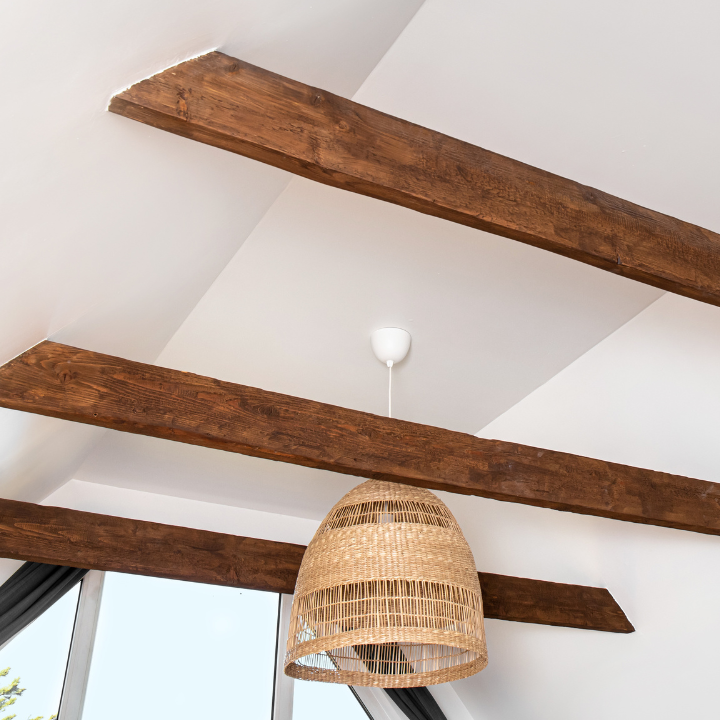 Vigas de madera sobre un techo blanco, con una lámpara colgante tejida colgando en el medio.