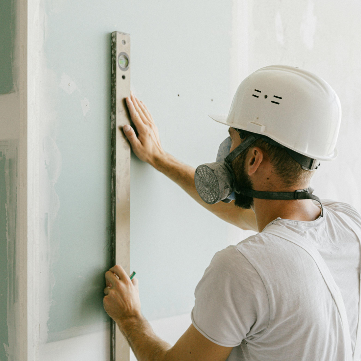 Trabajador de la construcción usando un nivel en una pared, usando un respirador y casco.
