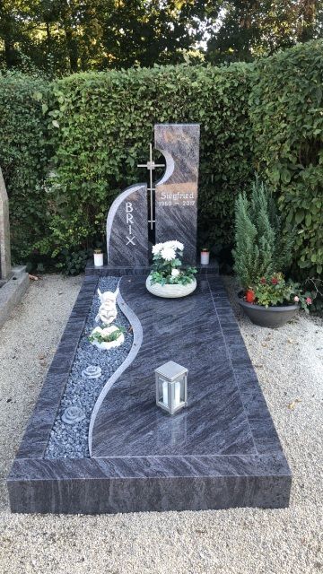 Grab mit Grabstein und Grabschmuck vor einer Hecke