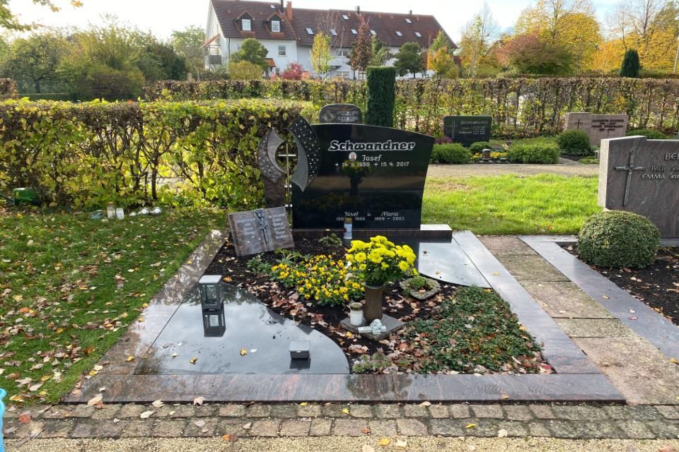 Grab mit Grabstein und Grabschmuck umgeben von einer Hecke und Wiese