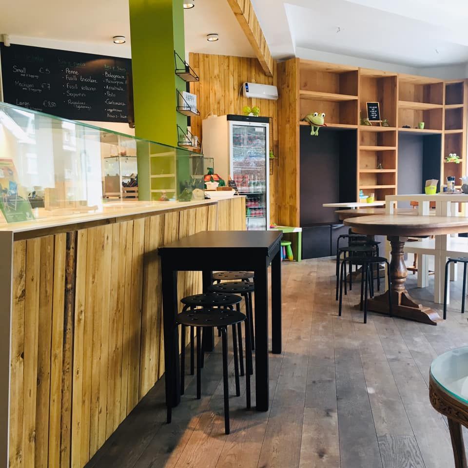 Interieur van een café met houten lambrisering, tafels, krukken en planken. Een koelkast en een krijtbordmenu zijn zichtbaar.