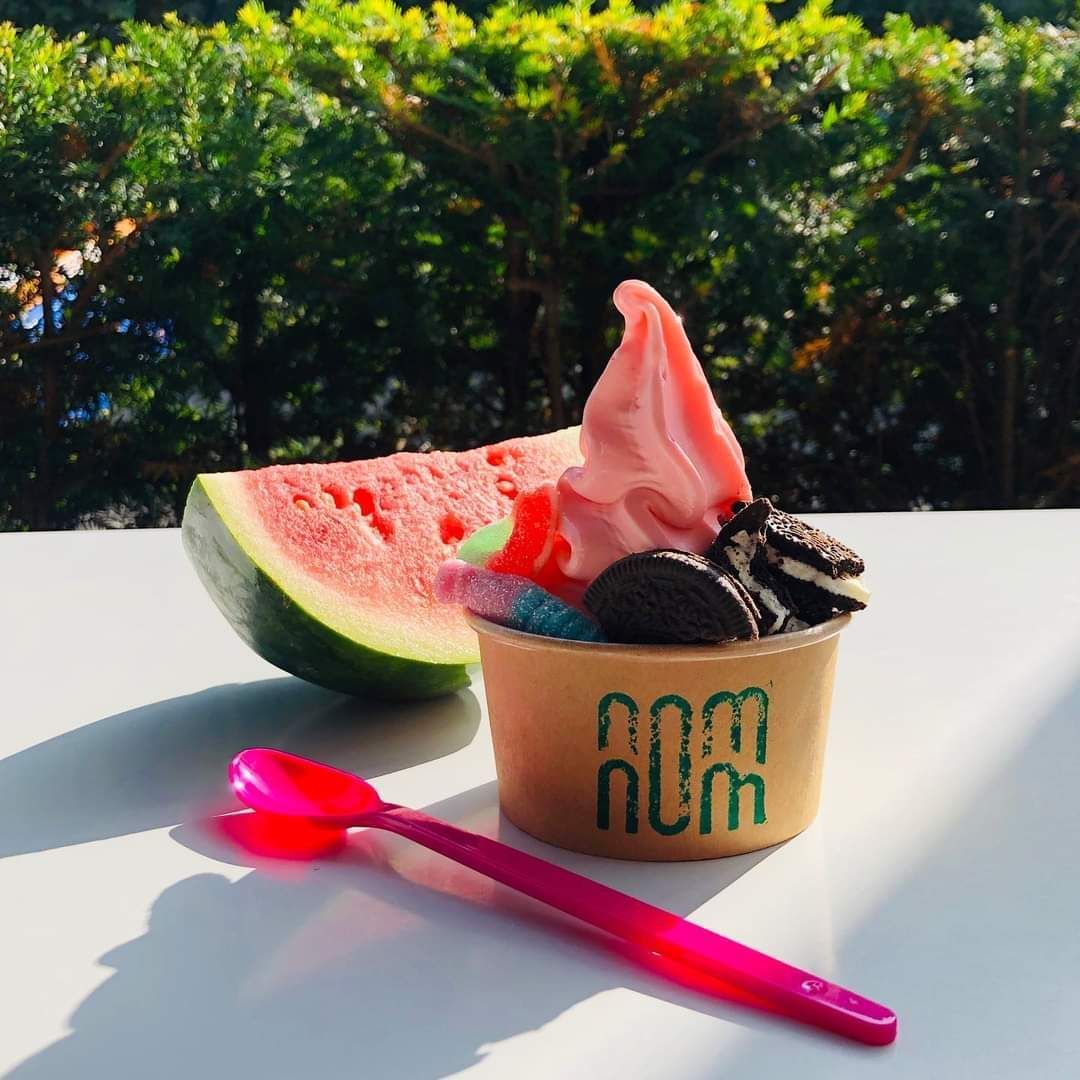 Roze softijs met watermeloen, koekjes en een lepel op een witte tafel.