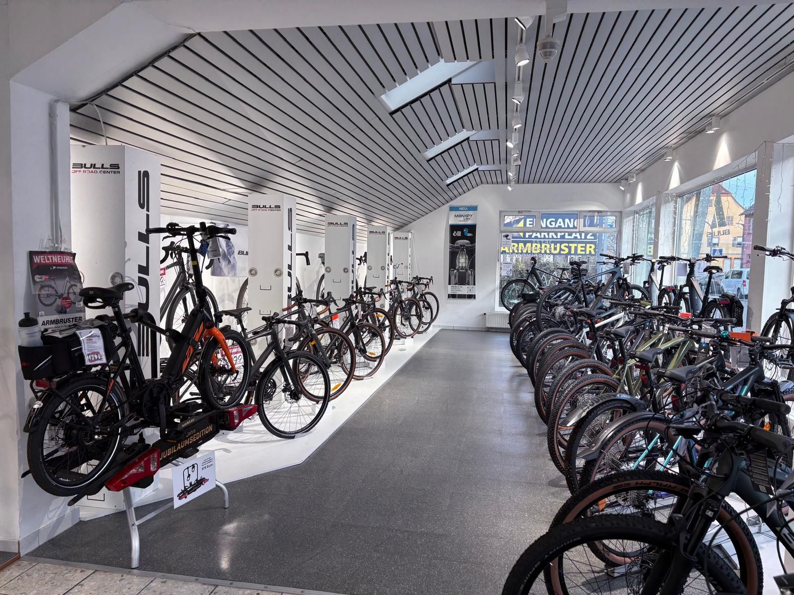 Das Interieur eines Fahrradgeschäfts mit Reihen von Fahrrädern, die unter hellem Deckenlicht auf dem Boden und an der Wand ausgestellt sind.