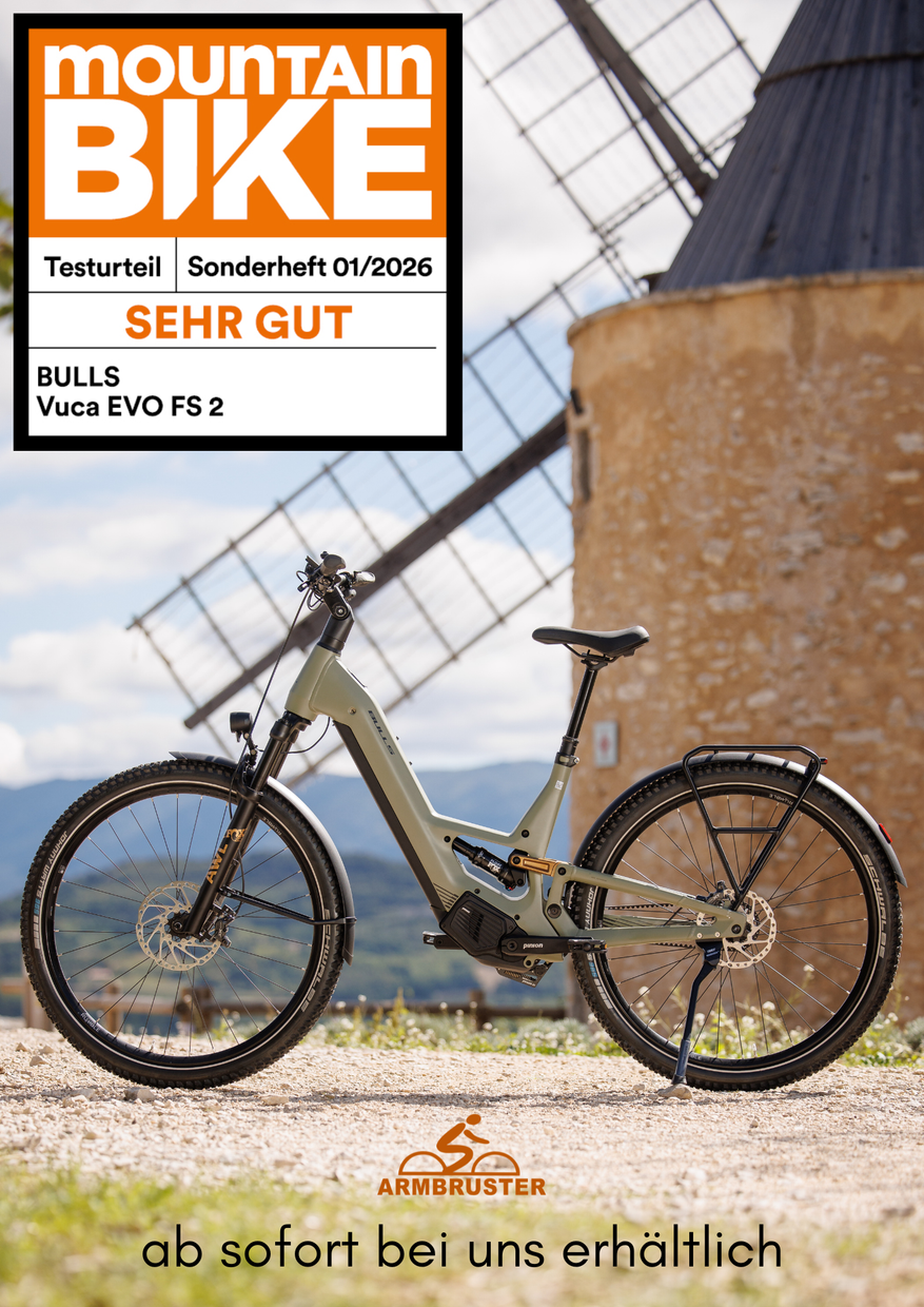 Ein Mountainbike lehnt an einer Windkraftanlage, daneben der orangefarbene Werbetext „MOUNTAIN BIKE“ und das Emblem „SEHR GUT“.
