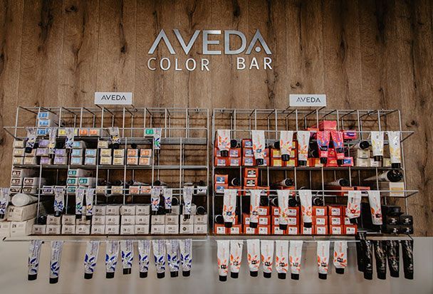 Expositor AVEDA Color Bar con diversos productos de coloración capilar. Fondo de pared de madera.