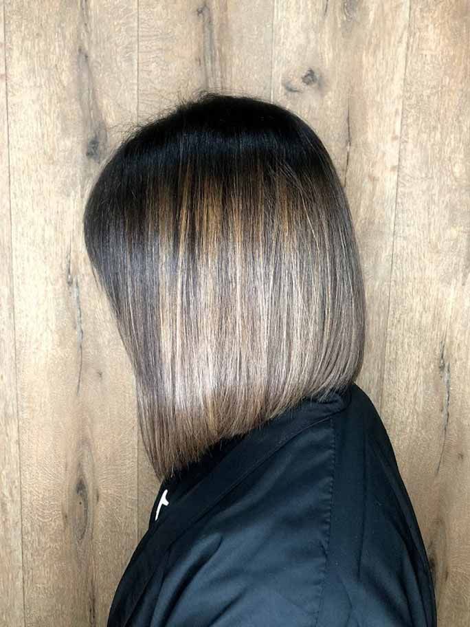 Una persona con un corte de pelo bob ombré de oscuro a claro frente a una pared de madera.