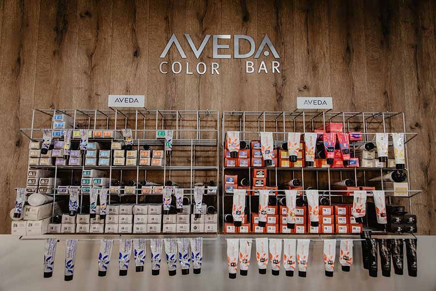 Exhibición Aveda Color Bar con productos para teñir el cabello en estantes, fondo de madera.