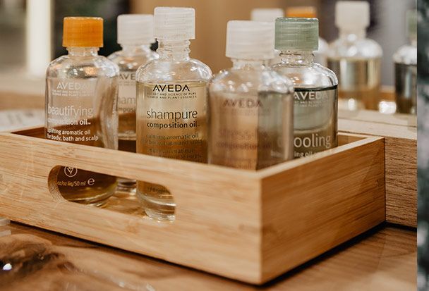 Pequeñas botellas de champú y acondicionador Aveda en una bandeja de madera.