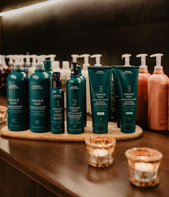 Productos para el cuidado del cabello en botellas de color verde azulado en exhibición de madera, con candelabros.