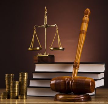 Libros de leyes con mazo, balanza de la justicia y monedas apiladas sobre un fondo oscuro.