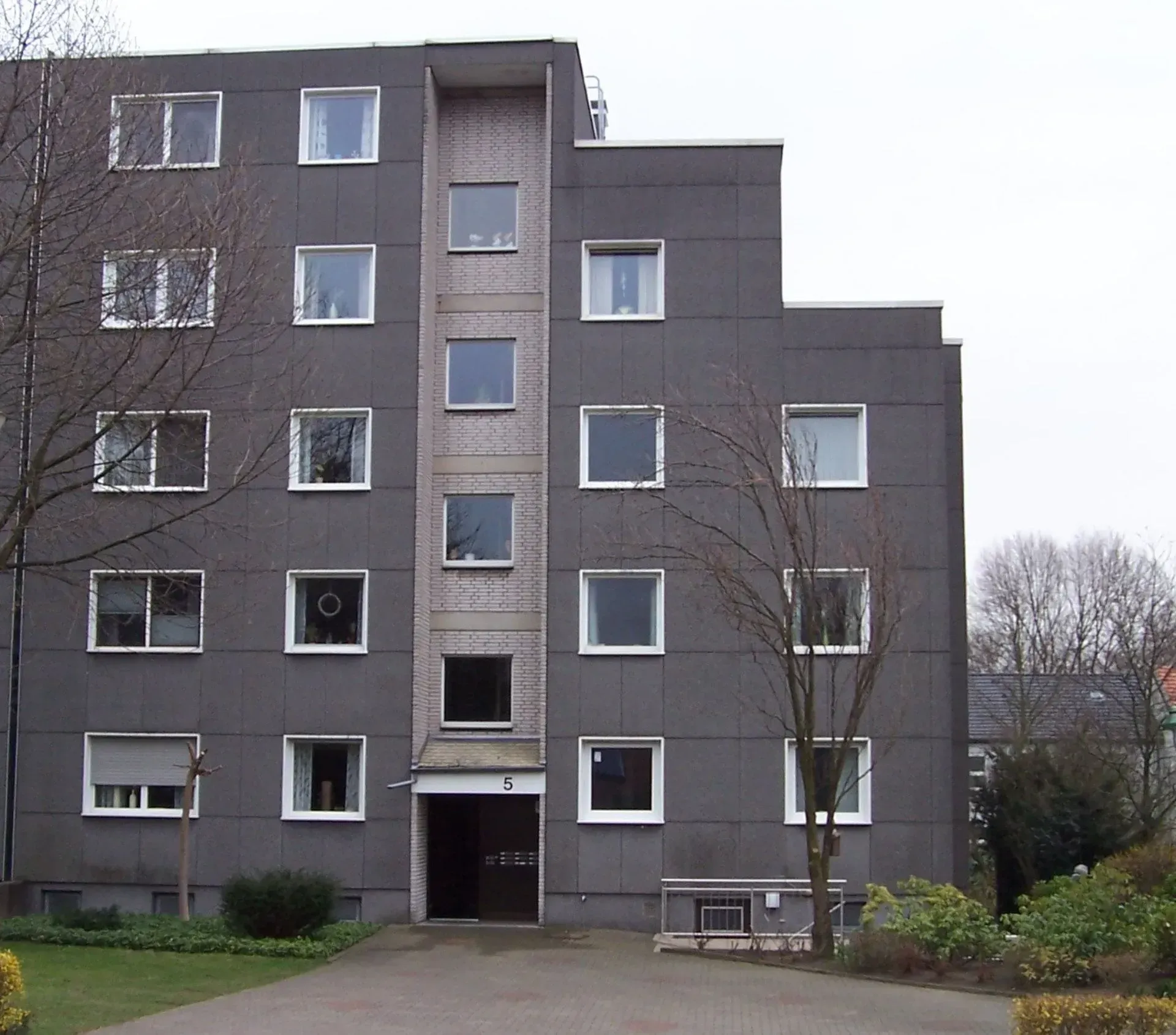 Ein graues Mehrfamilienhaus mit vielen Fenstern trägt die Nummer 5