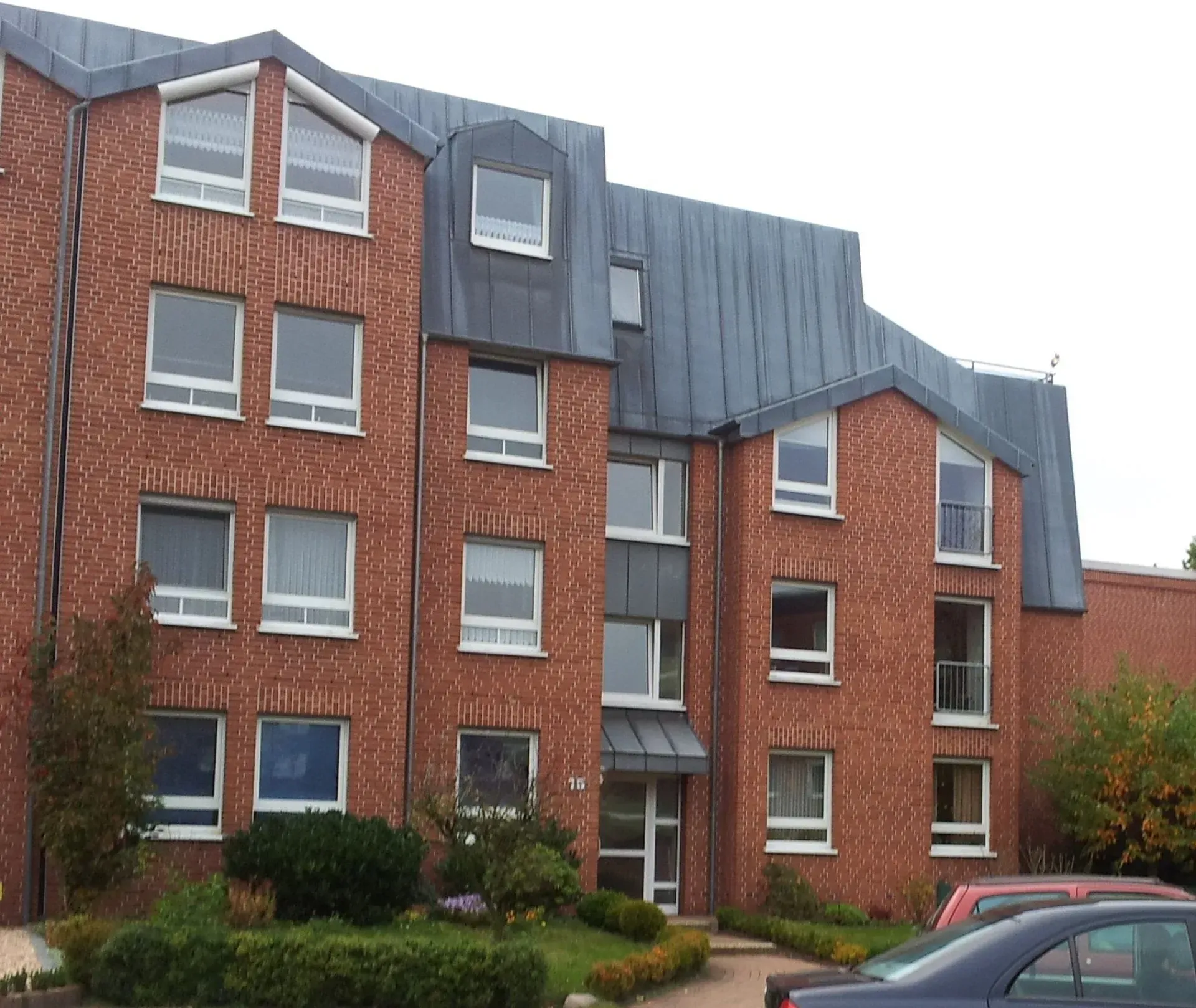 Ein großes Mehrfamilienhaus mit vielen Wohnungen und davor geparkten Autos