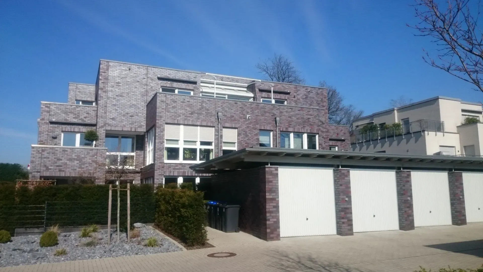 Ein großes modernes Mehrfamilienhaus mit eigenen Garagen davor, im Neubaugebiet