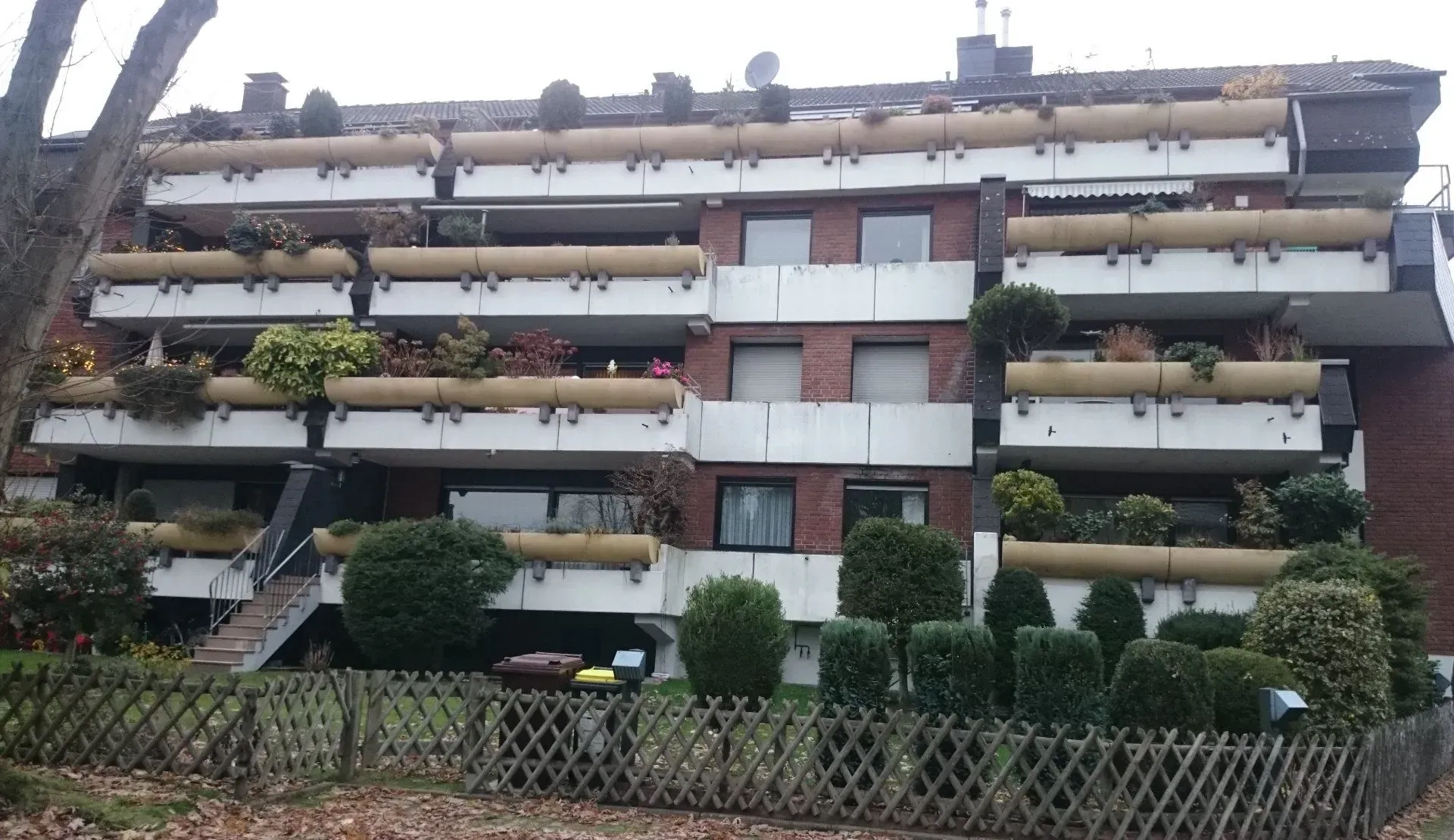 Ein großes Mehrfamilienhaus mit vielen breiten Balkonen und einer Treppe in den Garten