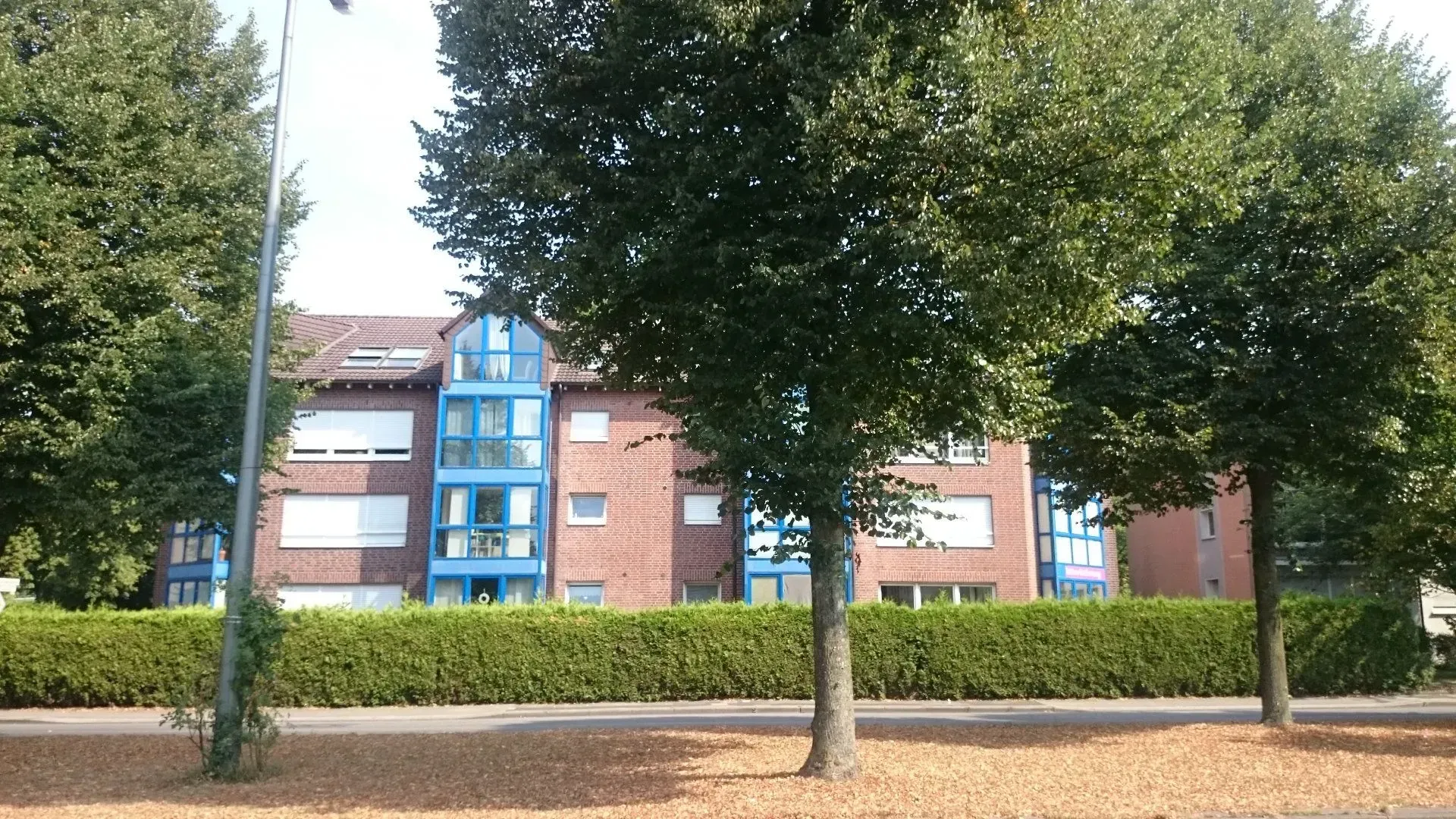 Ein Mehrfamilienhaus mit blauen Fensterfronten ist von Bäumen umgeben