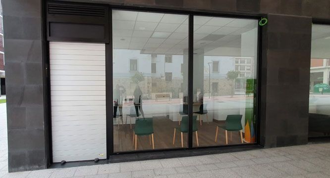 Un escaparate con una persiana blanca y sillas delante.