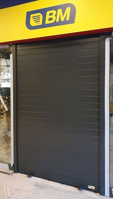 Un frente de tienda con una puerta de garaje negra y un cartel amarillo.