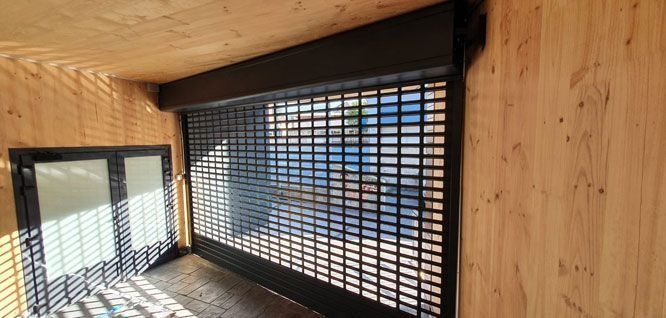 Una habitación con paredes de madera y una persiana negra en la puerta.