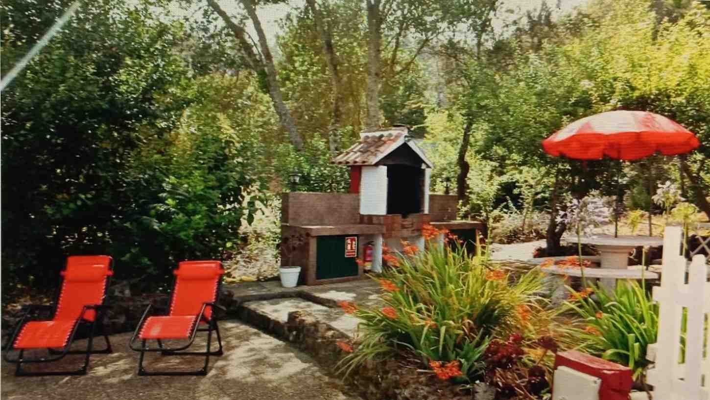 Escena de patio trasero con sillones rojos, área de parrilla, mesa de picnic y árboles.