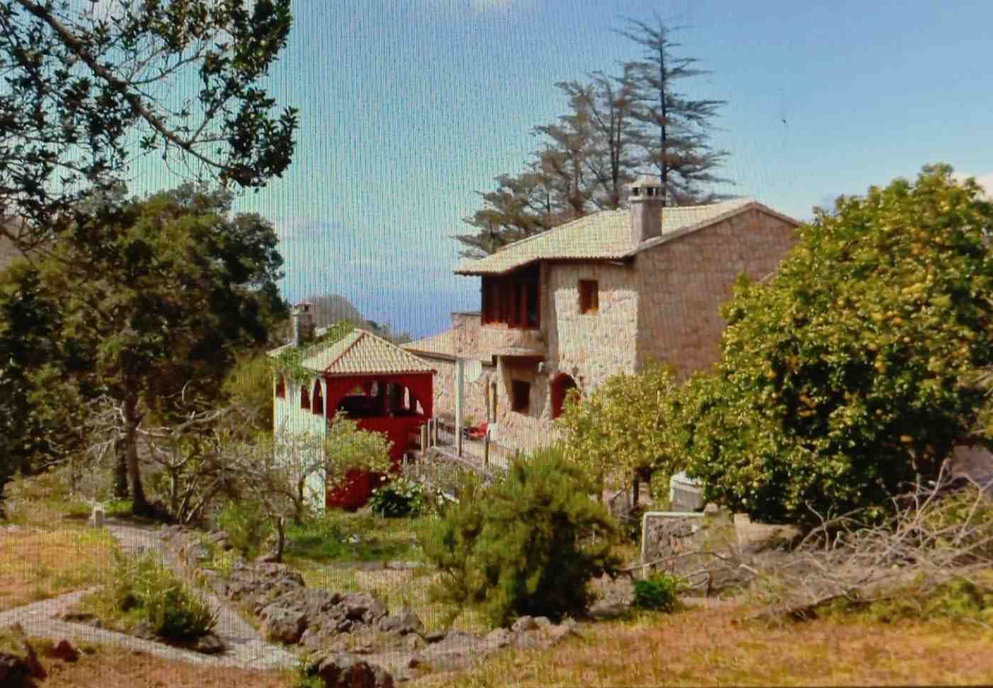 Edificio de piedra con detalles en rojo, rodeado de árboles y un camino de tierra.