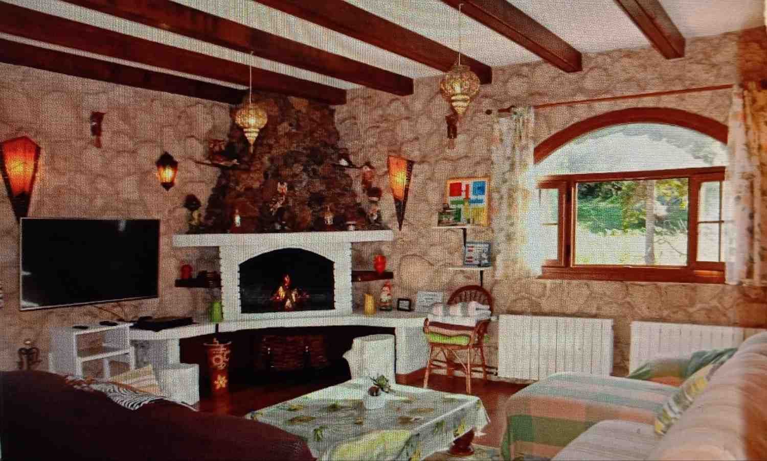 Sala de estar rústica con paredes de piedra, chimenea y ventana arqueada.