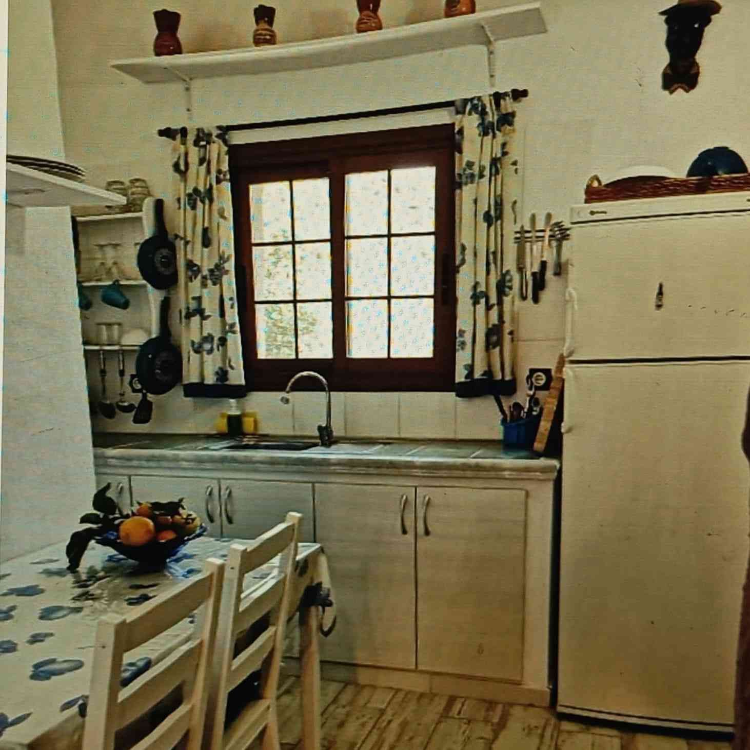 Una cocina rústica con gabinetes blancos, una ventana y una mesa puesta con frutas.