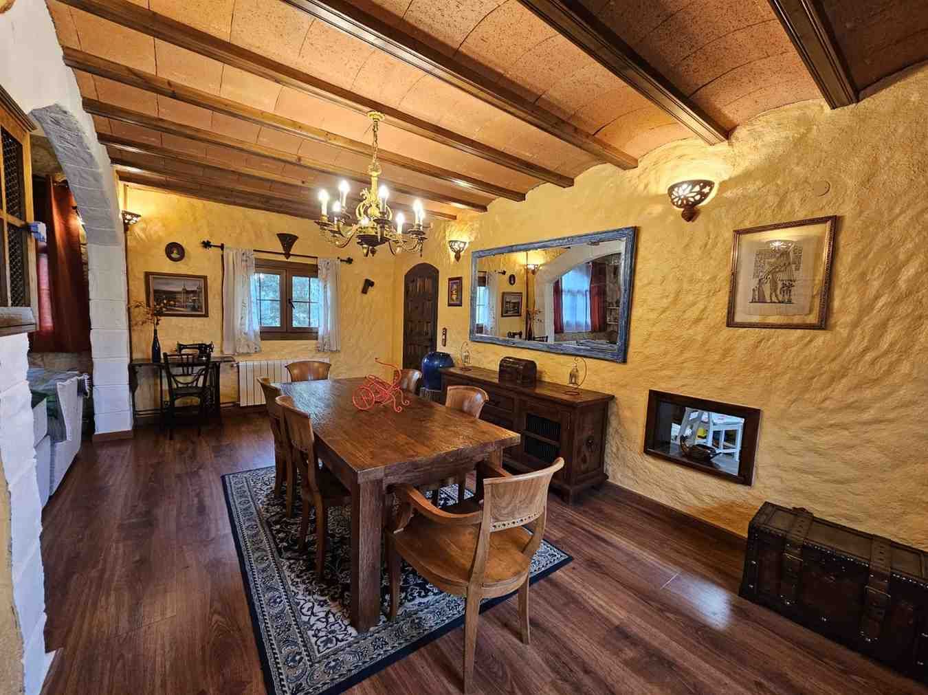 Comedor con mesa, sillas y candelabro de madera; paredes texturizadas en amarillo, techo y piso de madera.