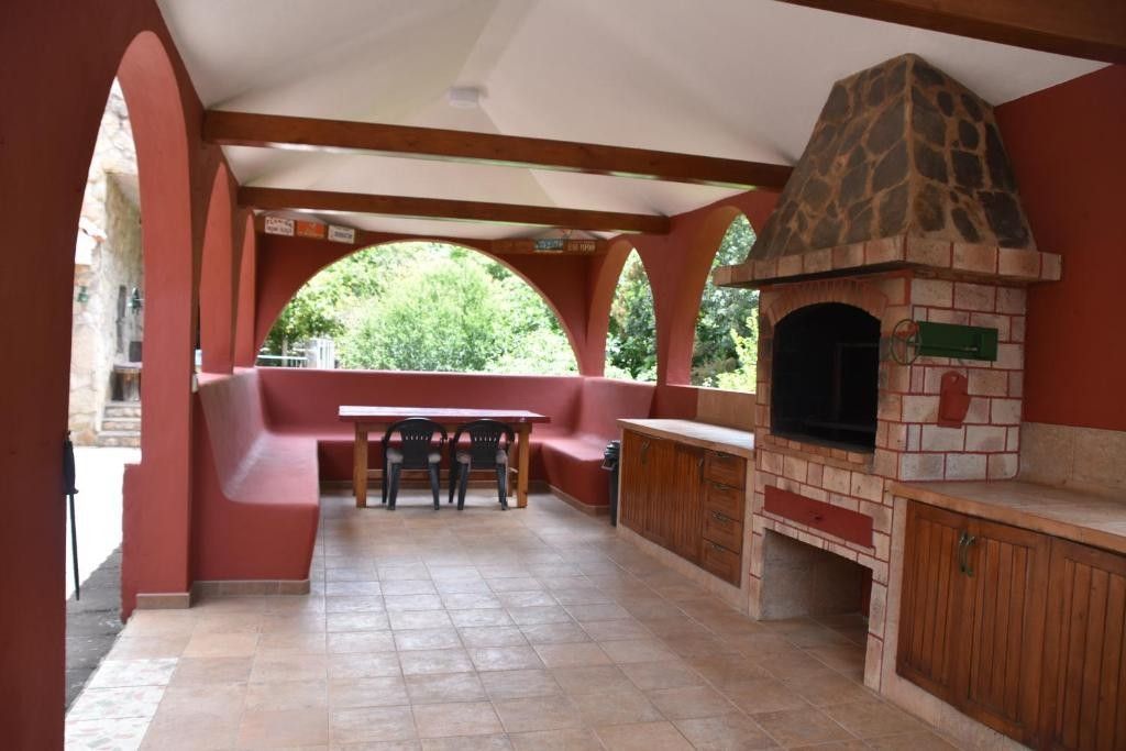 Comedor exterior cubierto con barbacoa incorporada, asientos y mesa bajo un techo arqueado.