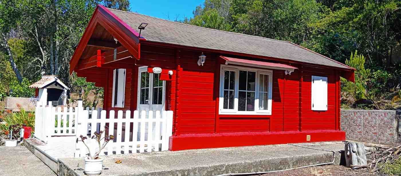 Casa de madera roja con valla blanca contra árboles verdes bajo un cielo azul.