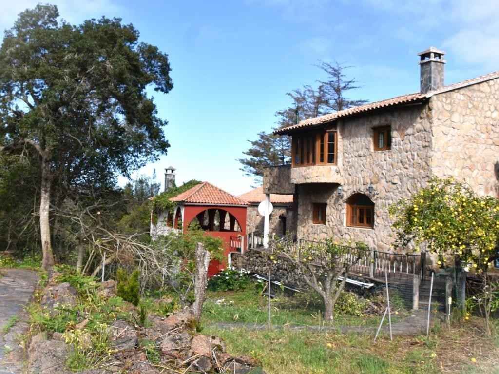 Casa de piedra con un edificio de techo rojo y un camino arbolado bajo un cielo azul.