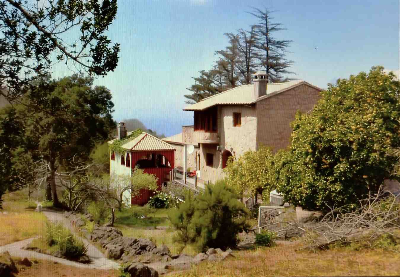 Casa de piedra con tejas de terracota, árboles y cielo azul.