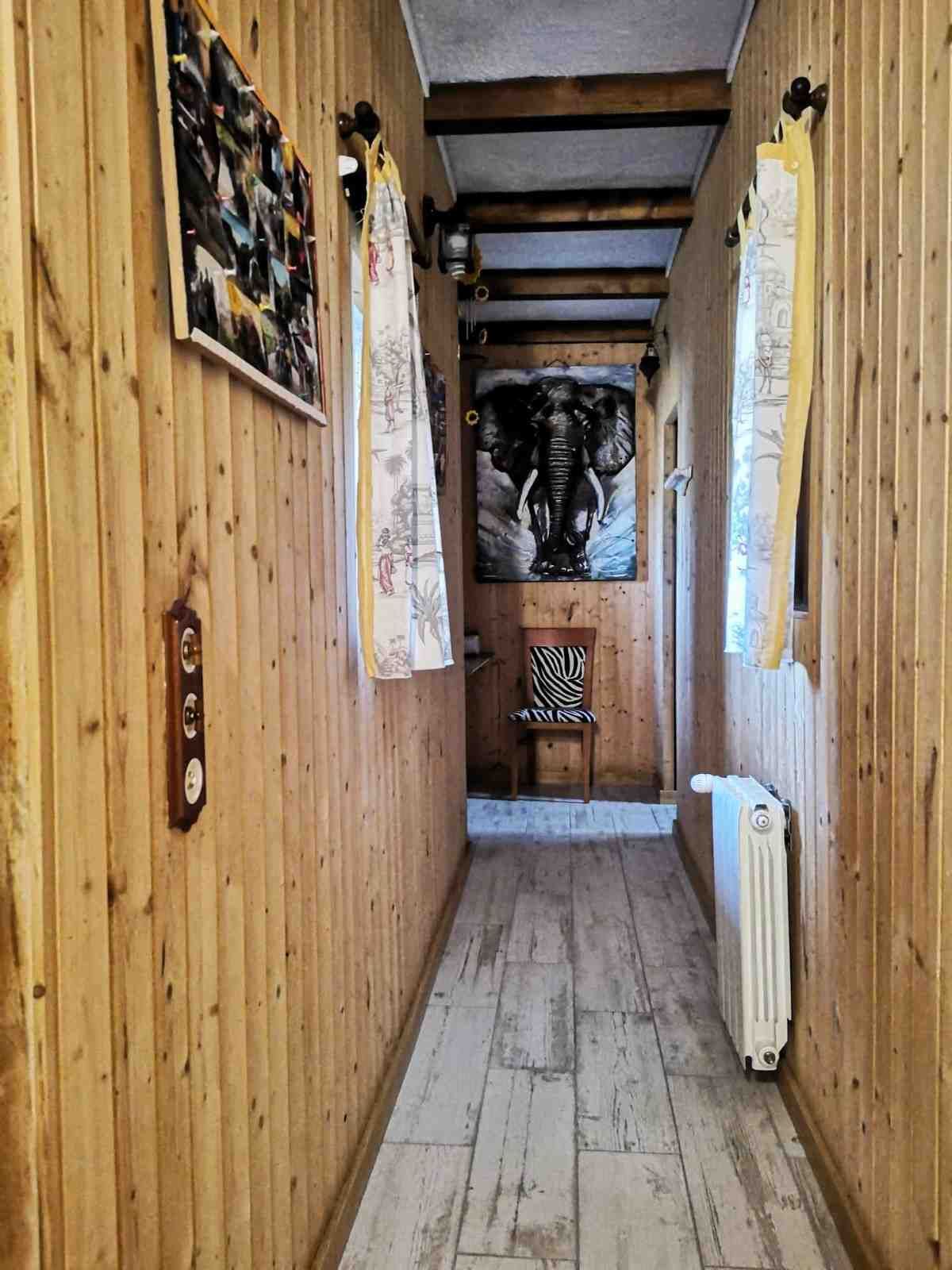 Pasillo estrecho con paredes y suelo revestidos de madera, obras de arte y un radiador.